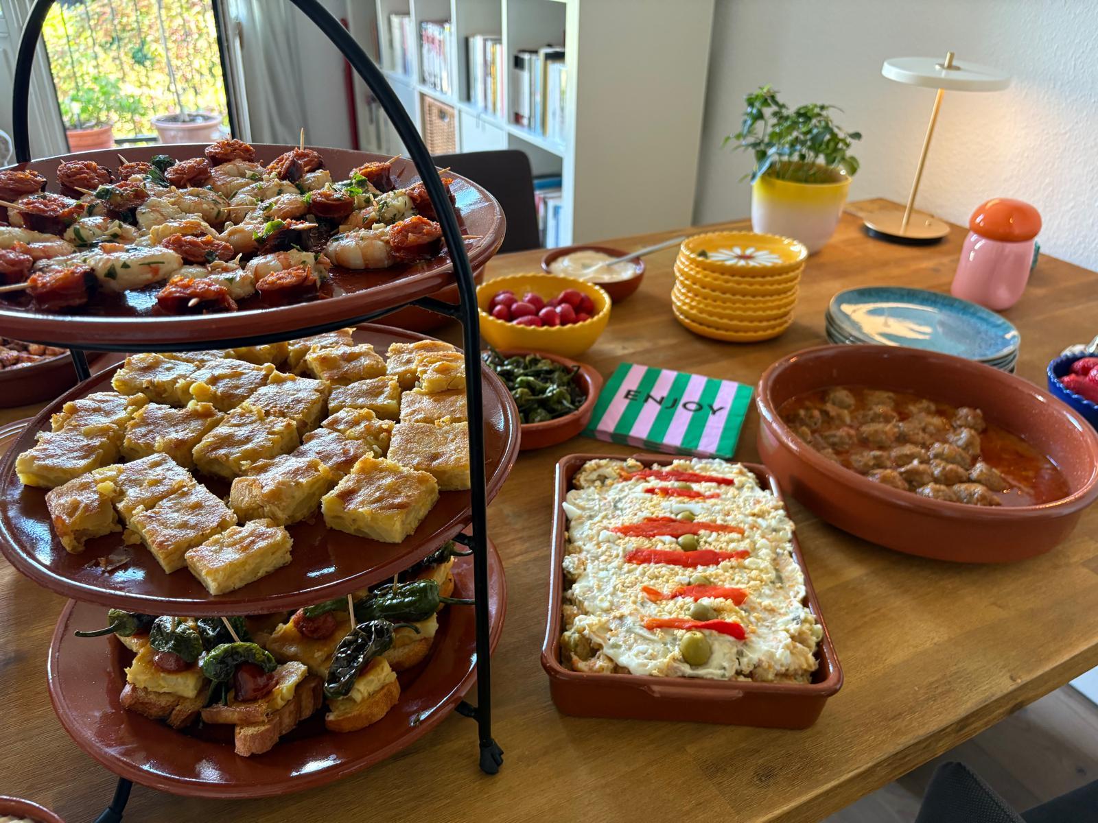 Tapas-Ständer mit Ensaladilla und Albóndigas auf gedecktem Tisch bei einer Geburtstagsfeier