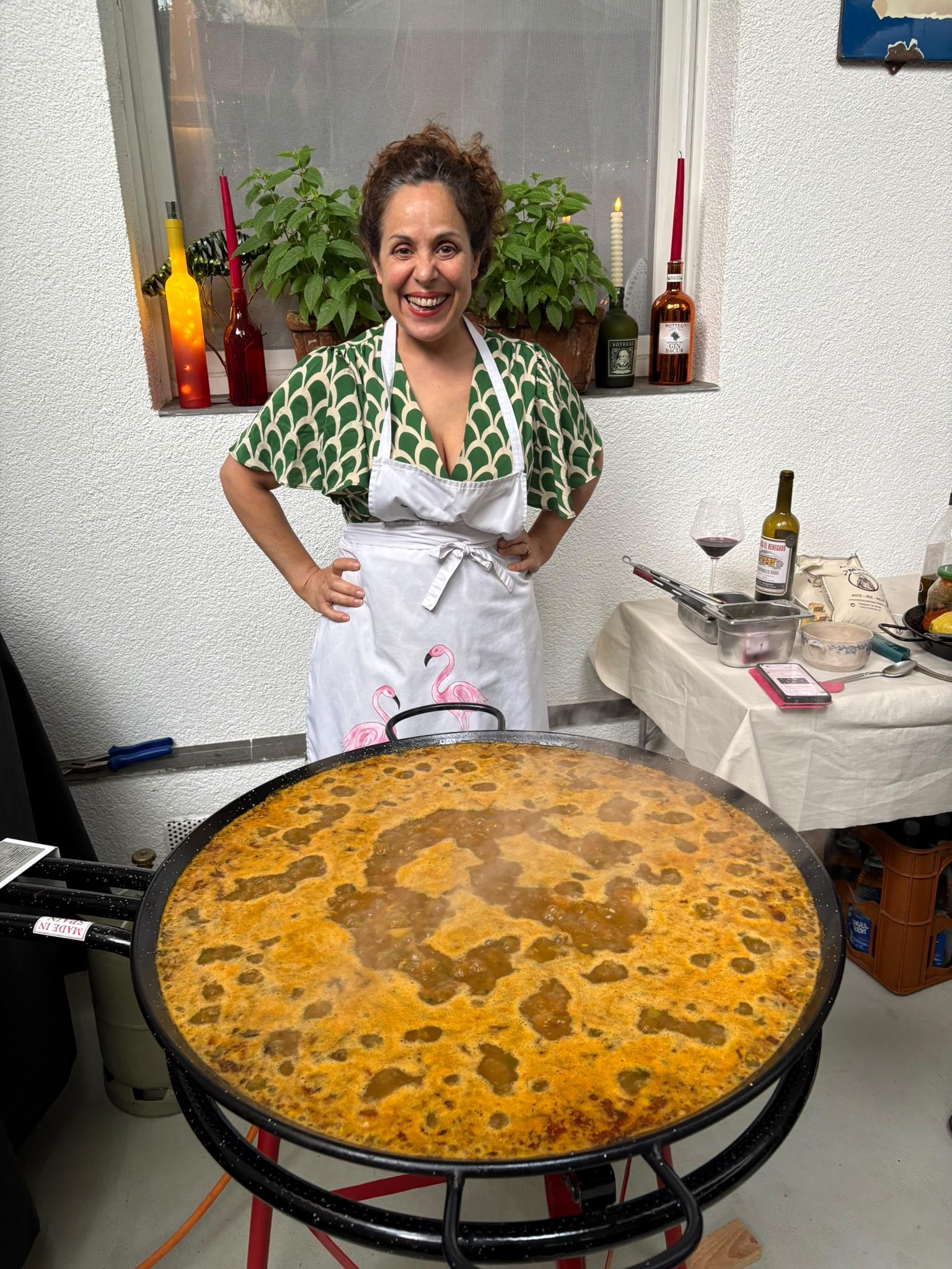 Julia Sanchez lächelt hinter einer riesigen, dampfenden Paella