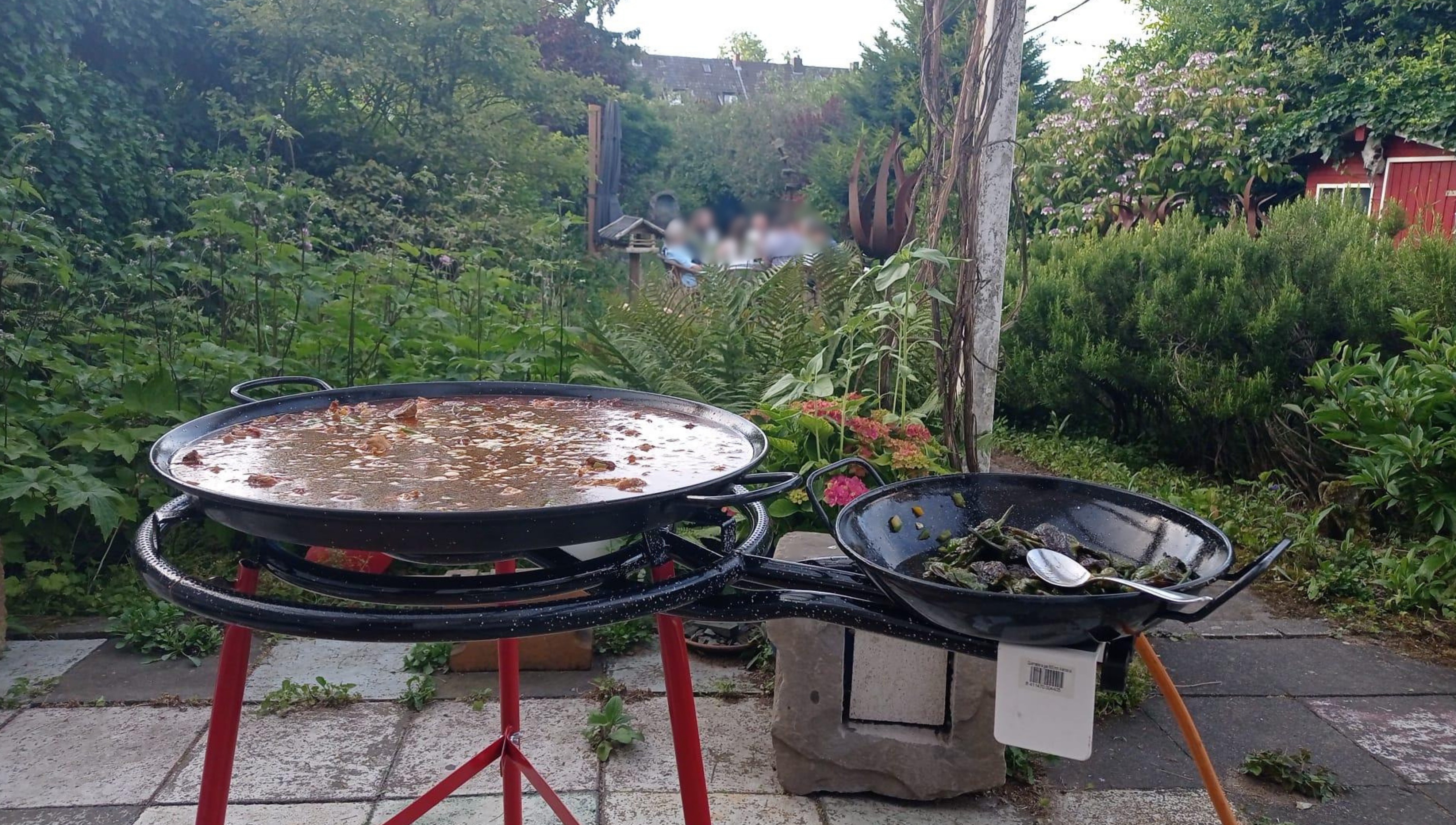 Zwei Paella-Pfannen köcheln im Garten auf Gasbrennern